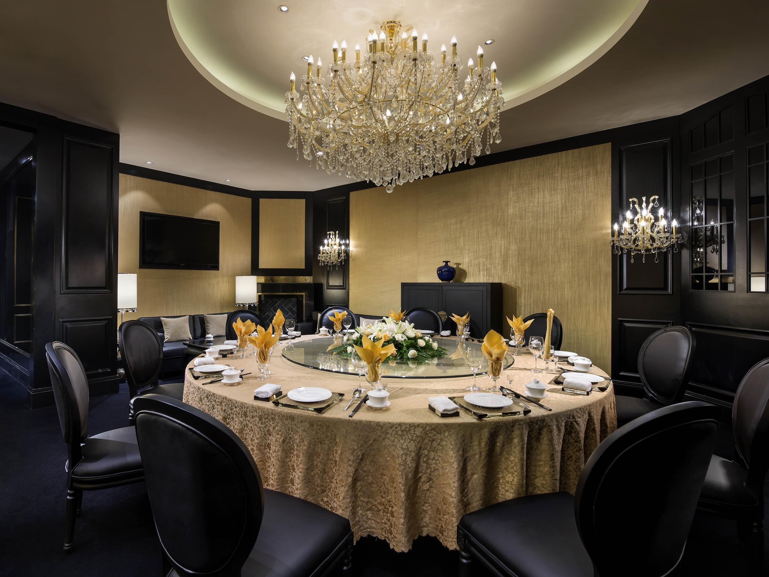 A formal dining room with a round table, black chairs, a chandelier, and a fireplace.