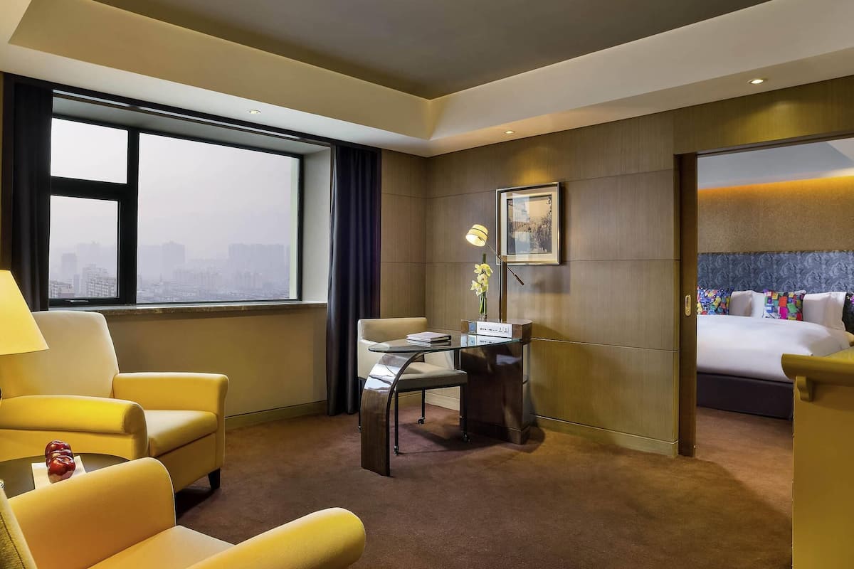 Habitación de hotel con vistas a la ciudad, un escritorio con lámpara, una cama con almohadones de colores y una silla.