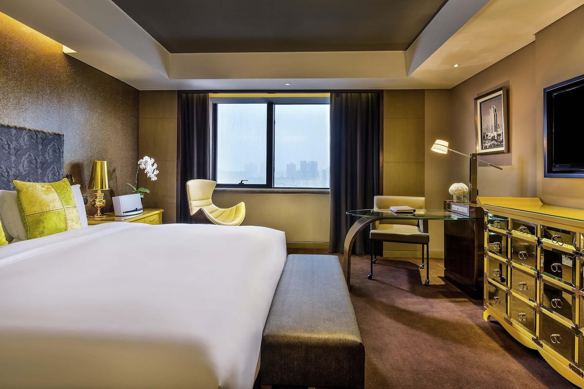 Habitación de hotel con una cama grande, un escritorio, una silla, un aparador y una ventana con vistas a la ciudad.