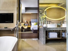 Quarto de hotel moderno com uma banheira grande, uma mesa com cadeira, uma cama e banheiro com toucador e pia.