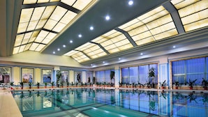 Una piscina interior con techo de vidrio, plantas en macetas a lo largo de las paredes y suelo de baldosas.