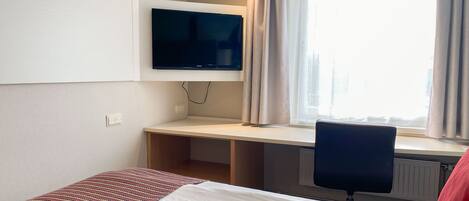 A hotel room with a bed, a desk, a chair, a television, and a window with curtains.