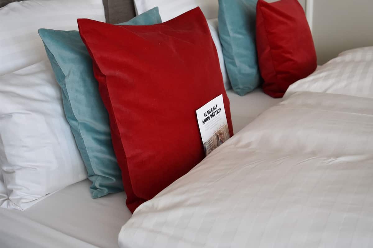 A neatly made bed with white bedding and multiple pillows in red and blue.