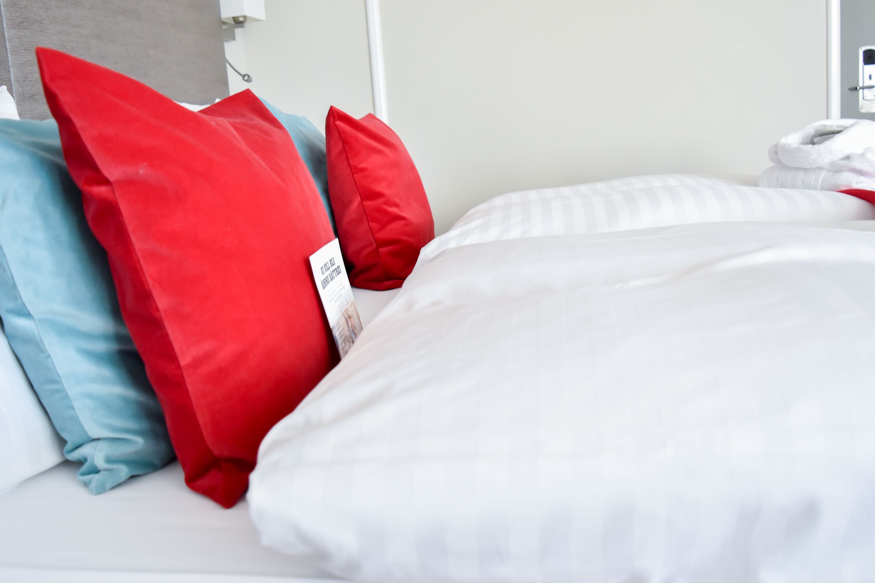 A neatly made bed with white and red pillows, a grey headboard, and a white wall.