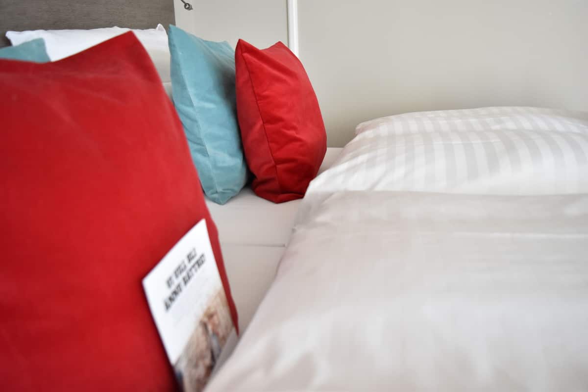 A bed with white bedding and three pillows in red, blue, and red.