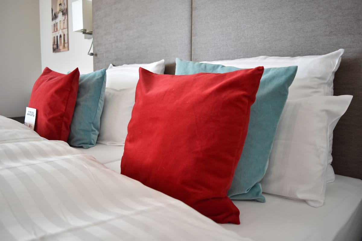 A bed with white bedding and pillows in red and teal colors.