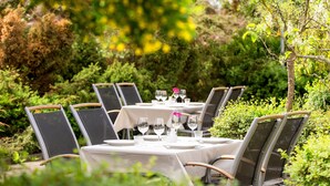 Un área de comedor al aire libre con mesas dispuestas para cuatro, rodeada de abundante vegetación.