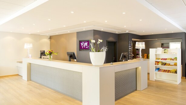 A reception desk with a large white vase of flowers, a digital screen, and a coffee machine. - Good Morning+ Hägersten (Hägersten)