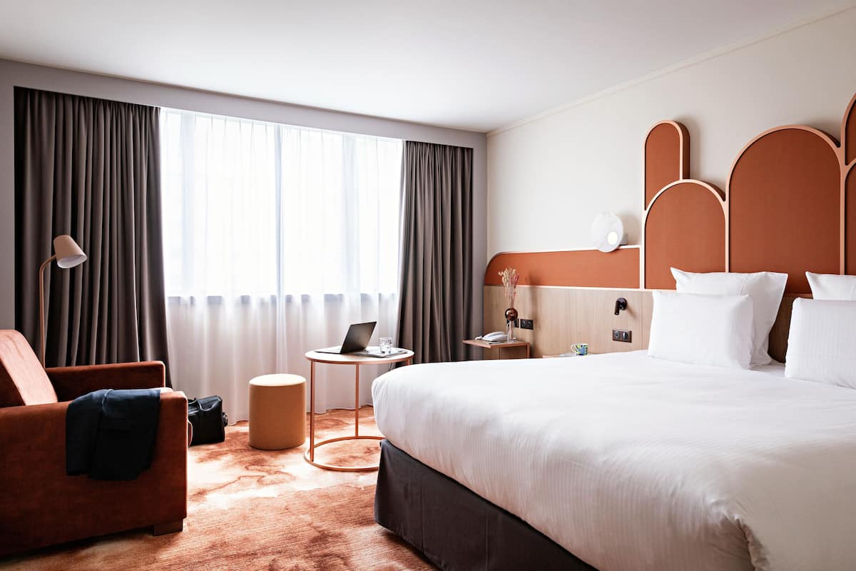 A modern hotel room with a large bed, a sofa, a desk, and a lamp.
