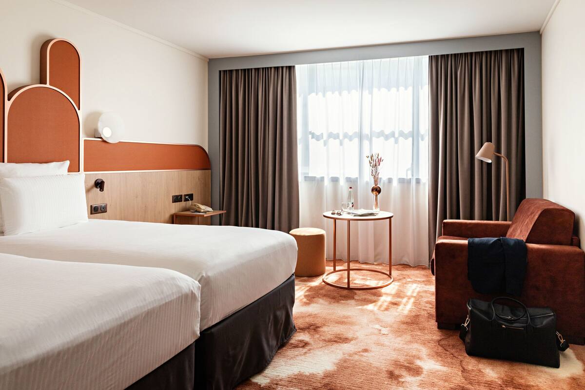 A hotel room with a large bed, a small table, a chair, and a suitcase.