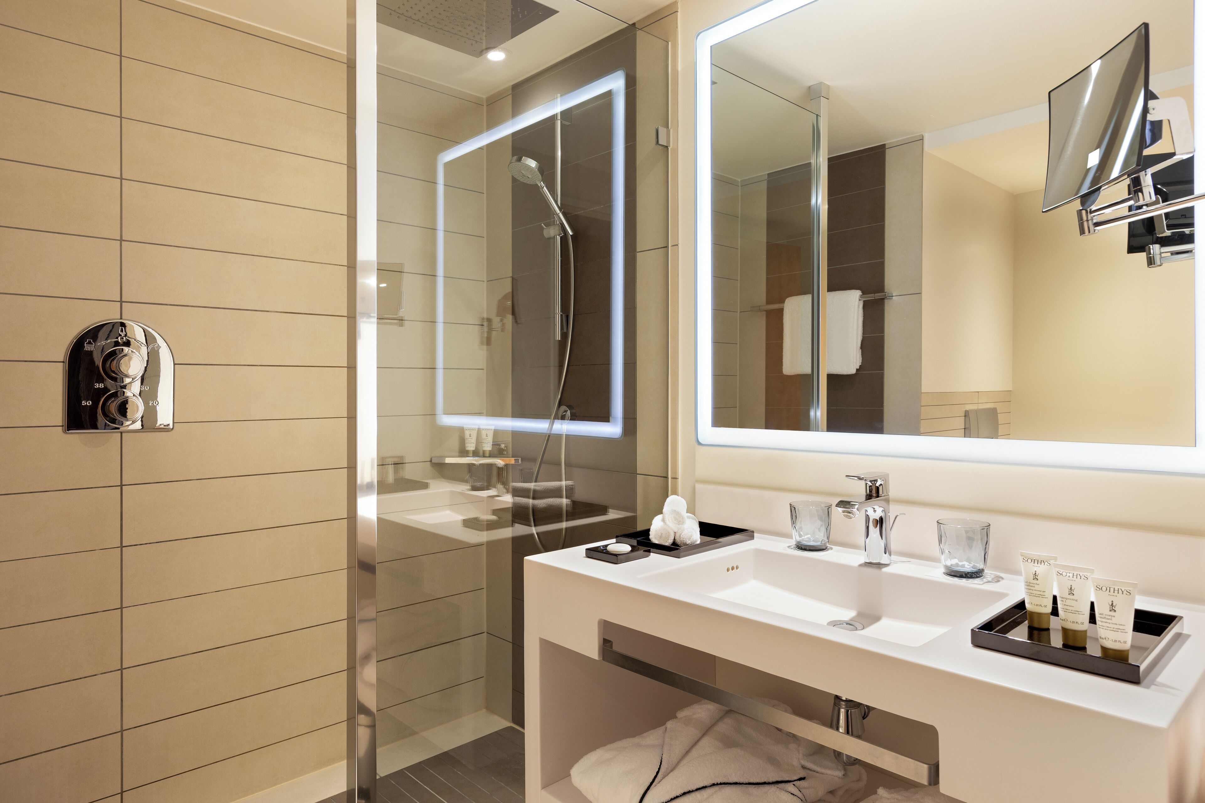A modern bathroom with a glass-enclosed shower, a large mirror, and a vanity with two sinks and toiletries.