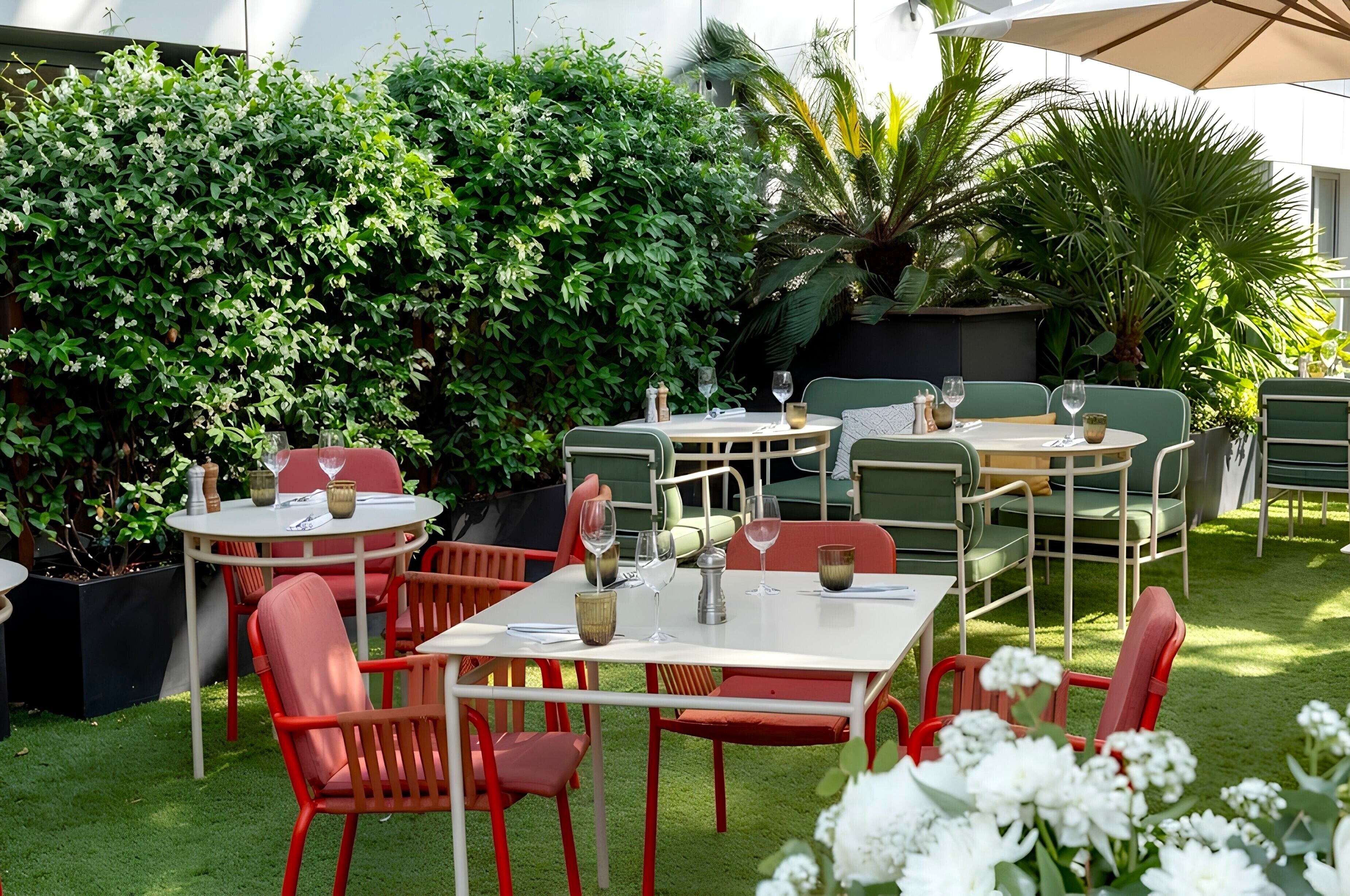 Un patio al aire libre con mesas y sillas, rodeado de abundante vegetación.