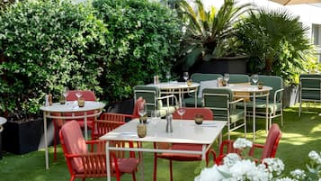 Un patio al aire libre con mesas y sillas, rodeado de abundante vegetación.
