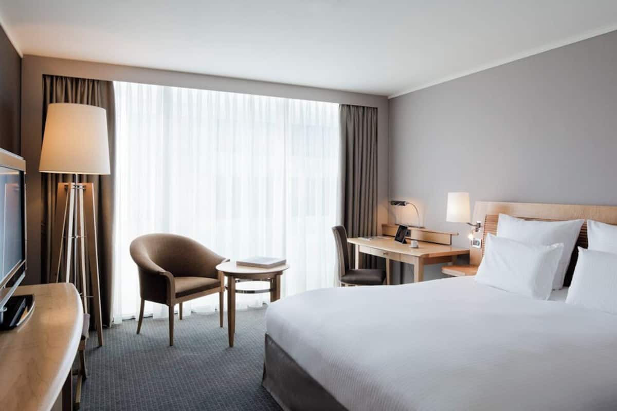 A hotel room with a bed, a desk, a chair, a TV, and a lamp.