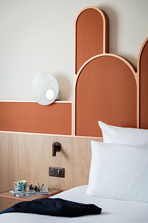 A hotel room with a wooden headboard, a bedside table with a cup, sunglasses, and a magazine, and a bed with white bedding. - Pullman Paris Centre-Bercy (Paris)