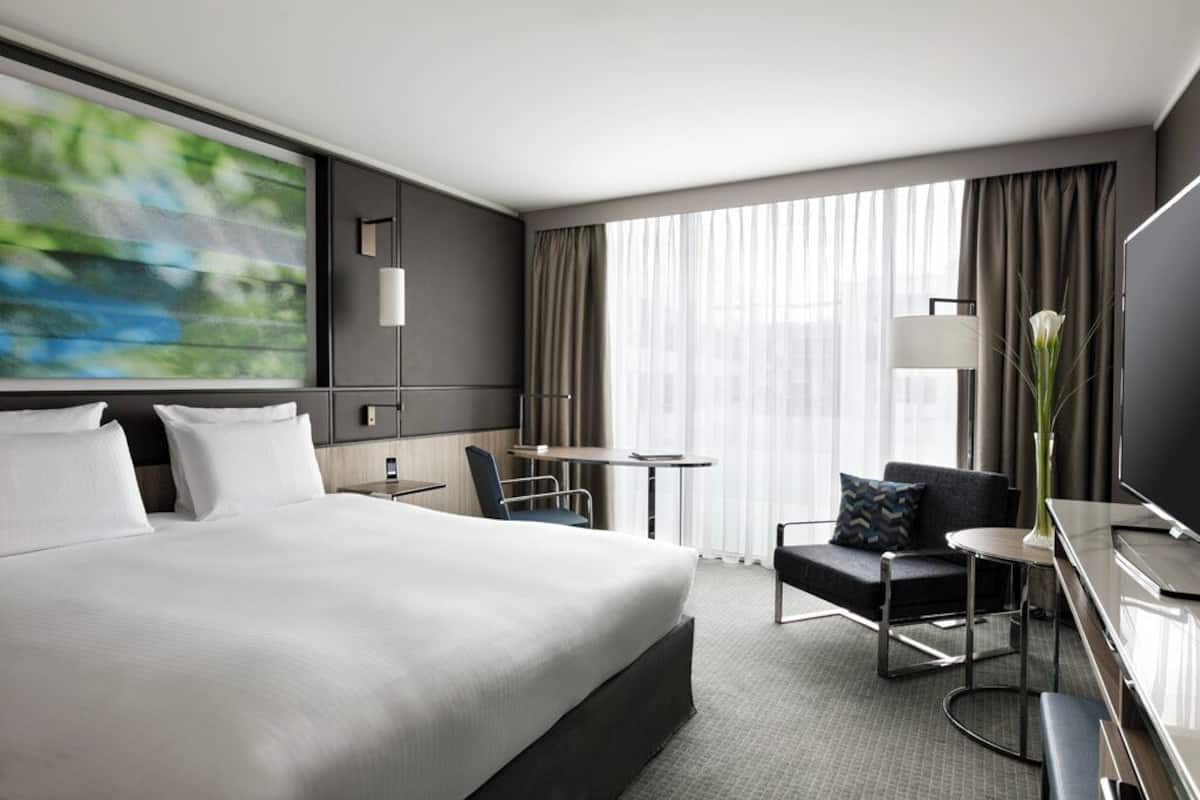 A modern hotel room with a large bed, a desk, a chair, and a TV.