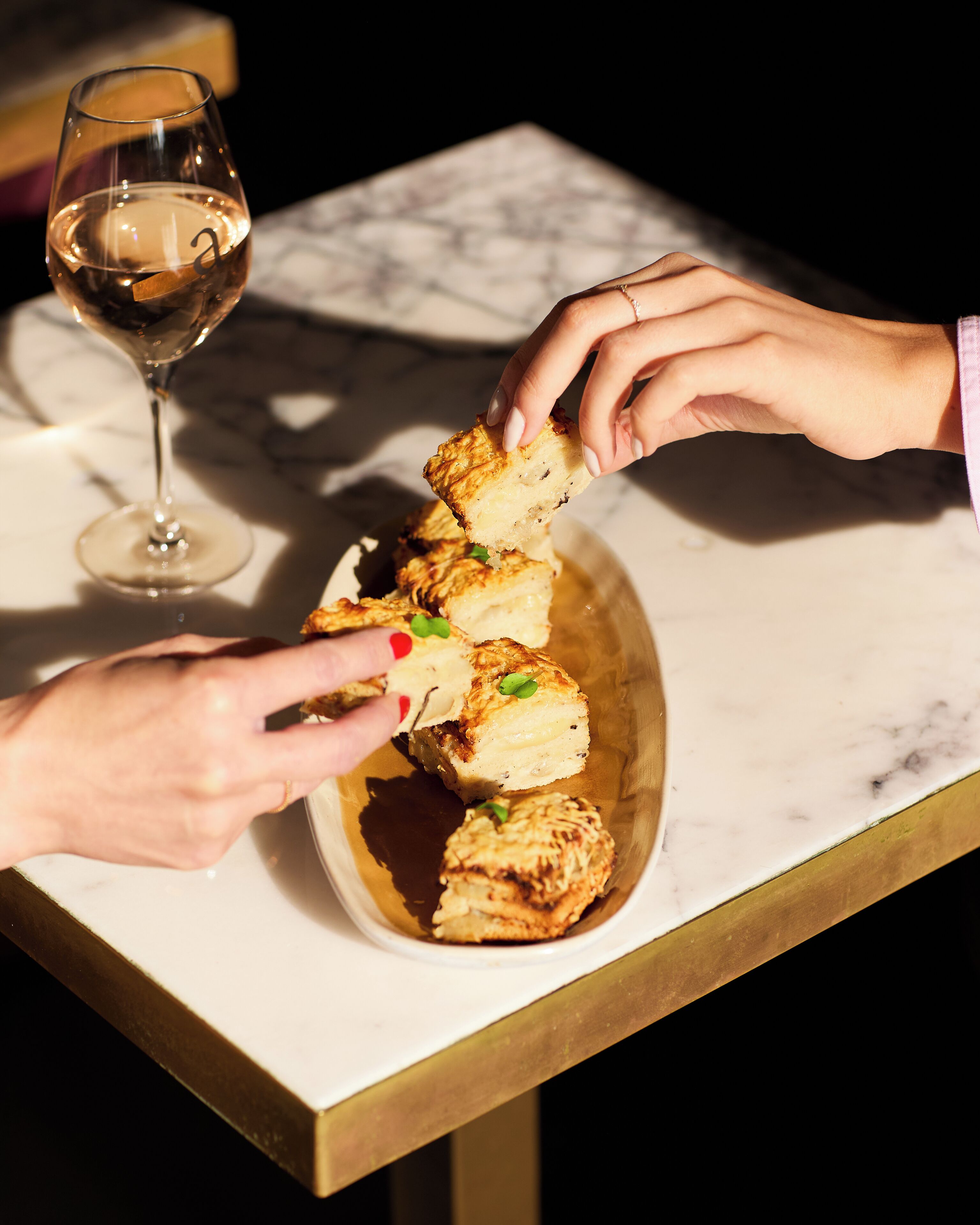 A marble table with a glass of white wine and a bowl of pastries.
