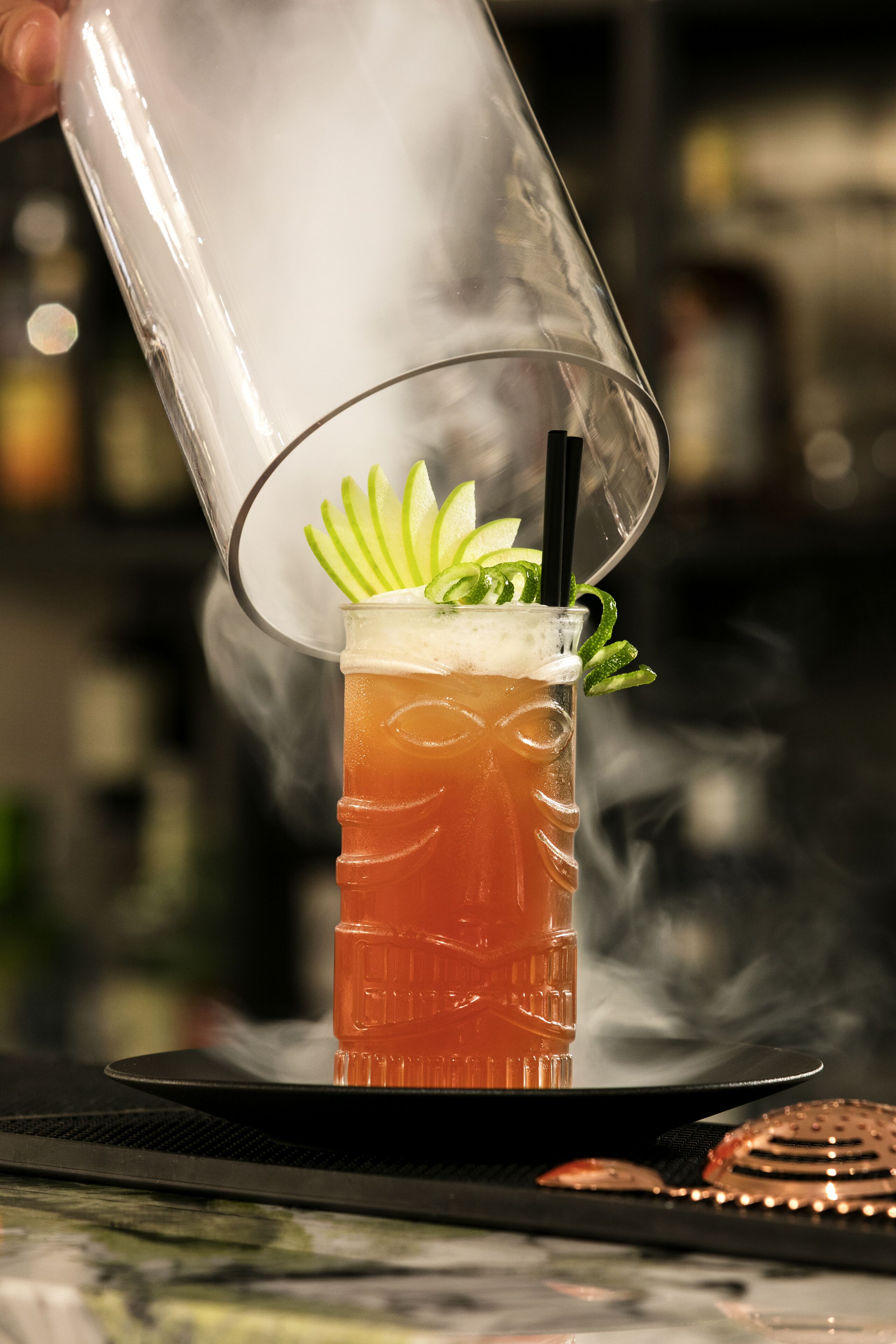 A cocktail being poured into a glass with a decorative garnish.