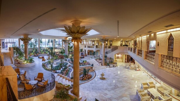 A spacious lobby with a central garden, multiple seating areas, and a grand staircase.