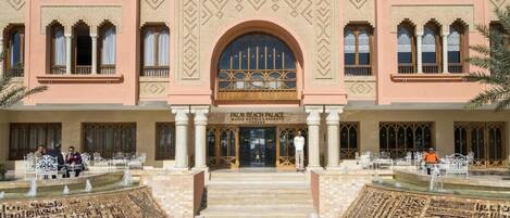 Palacio Palm Beach con una entrada central en arco, fachada simétrica y fuentes decorativas.