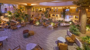 A spacious indoor atrium with multiple seating areas, a central water feature, and lush greenery.