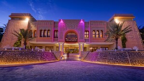 A grand entrance with a central archway, palm trees, and a paved area leading to the building.