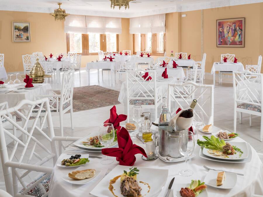 A formal dining room with white tables and chairs, arranged for a meal.