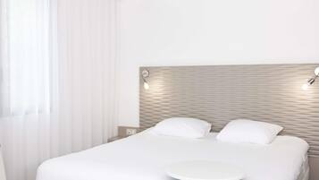 A modern hotel room with a large bed, a round bedside table, and a headboard with built-in lighting.