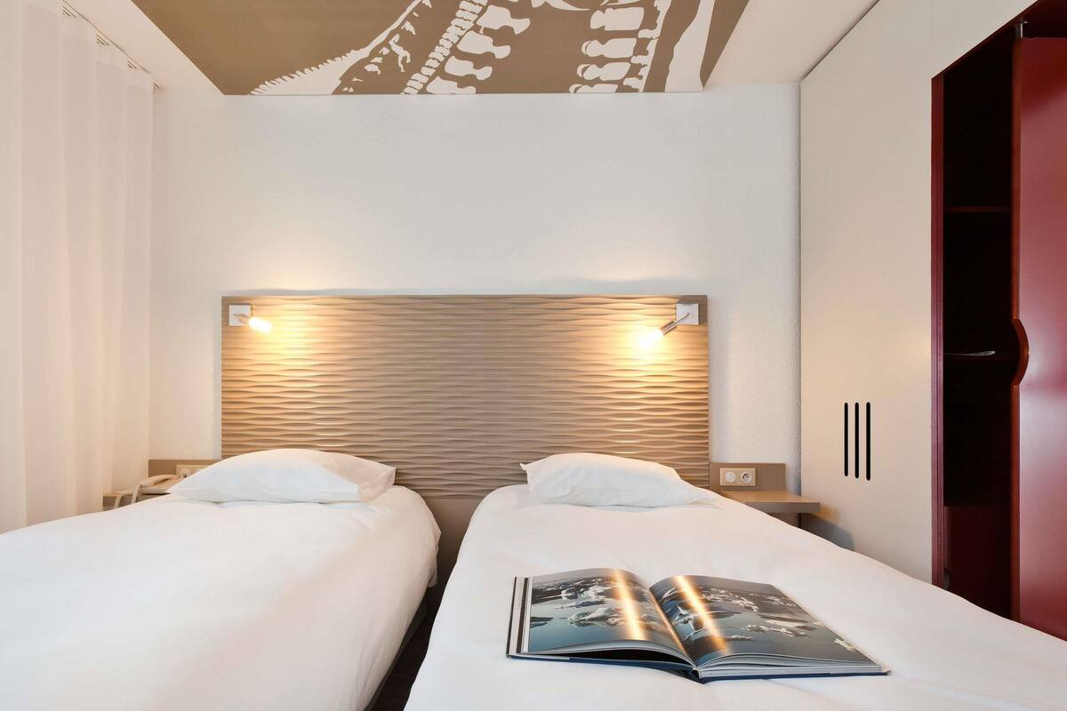 A hotel room with two single beds, a wooden headboard, bedside lamps, a nightstand, and a wardrobe.