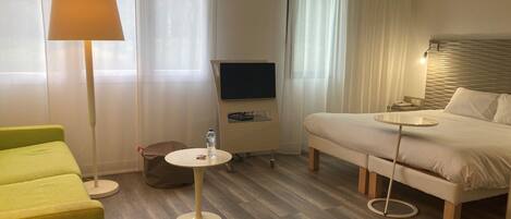 Habitación de hotel con cama, un sillón verde, una mesita redonda, televisión y lámpara.