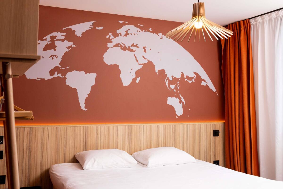 Quarto de hotel com uma cama, cabeceira de madeira, mapa-múndi na parede e luminária pendente.