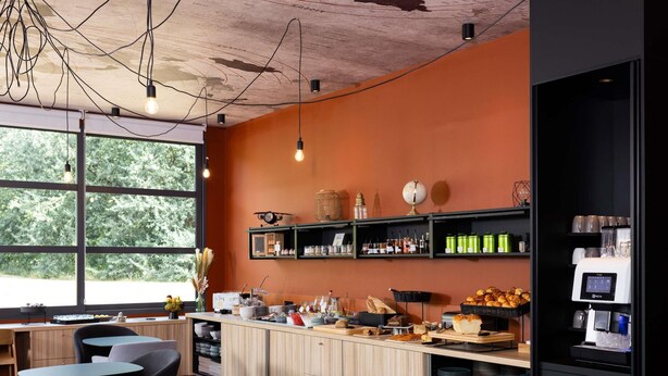 Un café moderne avec des meubles en bois, un coin bar et une grande fenêtre donnant sur les arbres.