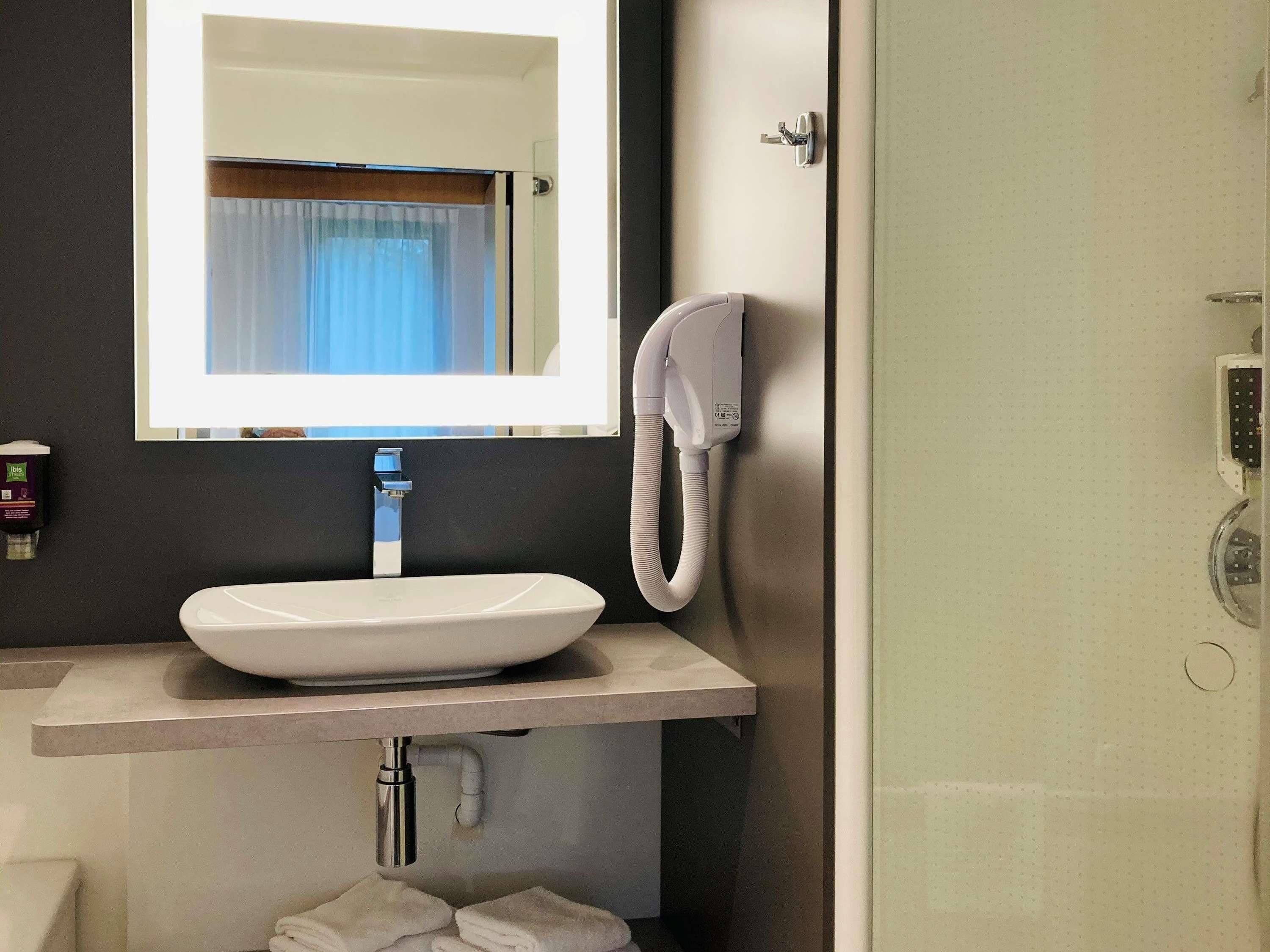 A bathroom with a white sink, a mirror, a hand dryer, and a towel rack.