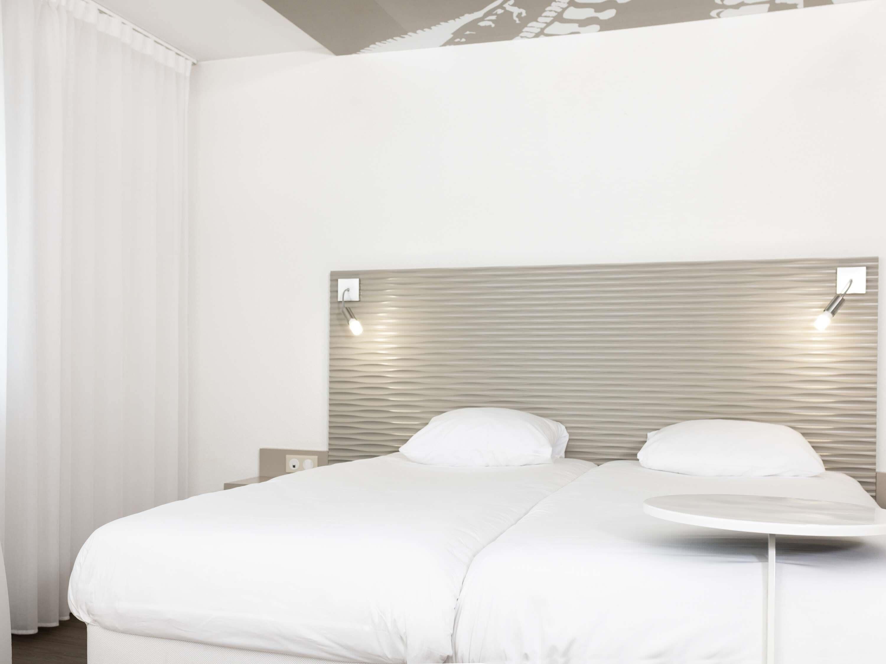 A modern hotel room with a large bed, a round table, and a headboard with built-in lighting.