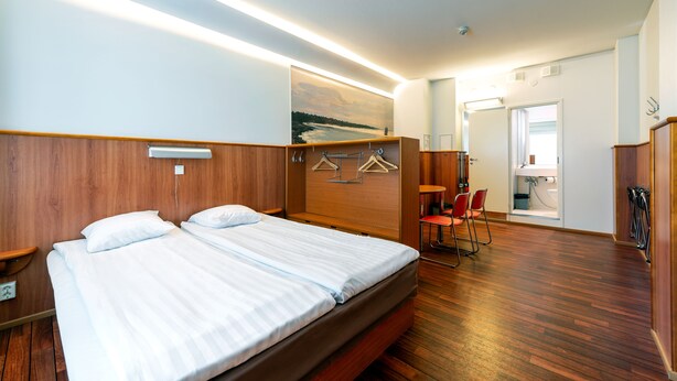 A hotel room with a wooden headboard, a bed with white linens, a wooden floor, a seating area with chairs, and a bathroom visible through an open door. - Omena Hotel Turku Humalistonkatu (Turku)
