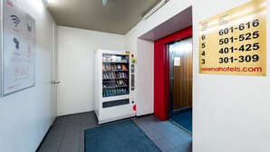 A hotel lobby with a vending machine, a red door, and a sign with room numbers and a website. - Omena Hotel Turku Humalistonkatu (Turku)