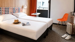 A hotel room with a bed, a small table, a chair, a suitcase, and a TV. - ibis Styles Caen Centre Historique (Caen)