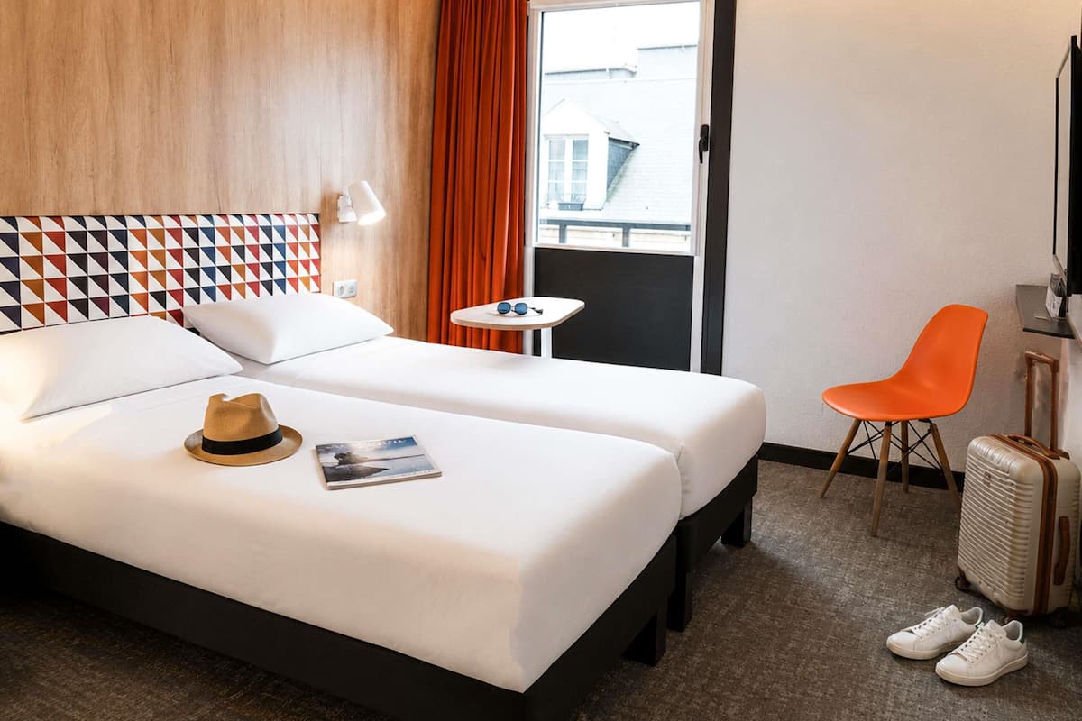 A hotel room with a bed, a small table, a chair, a suitcase, and a TV.