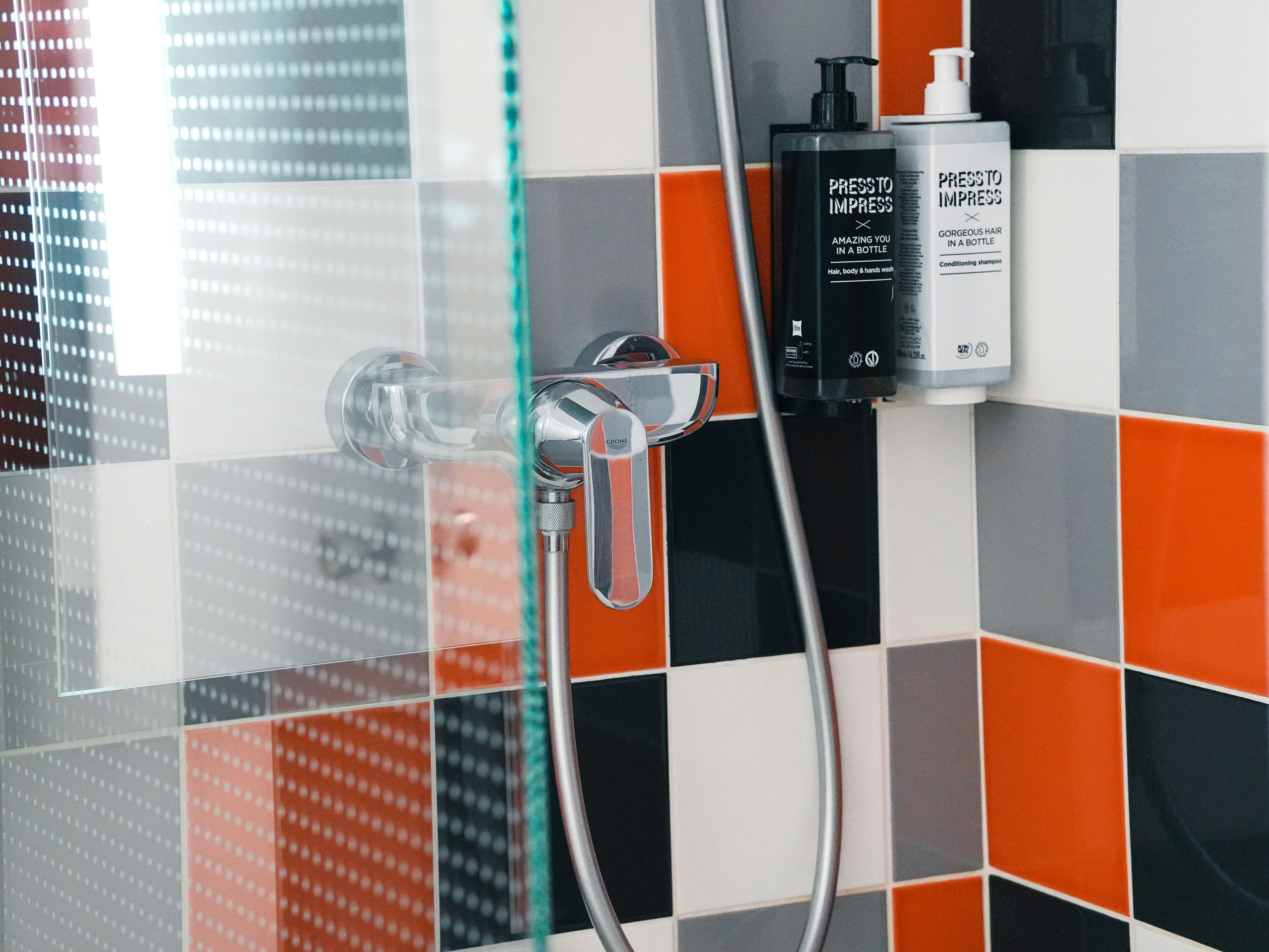 A shower with a chrome faucet and a glass door, a bottle of hair conditioner, and a bottle of body wash on the wall.