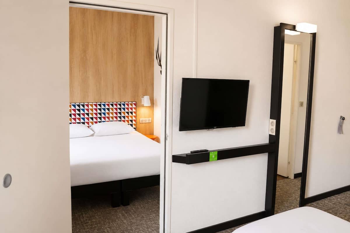 A hotel room with a bed, a TV mounted on the wall, a bedside table, and a mirror.