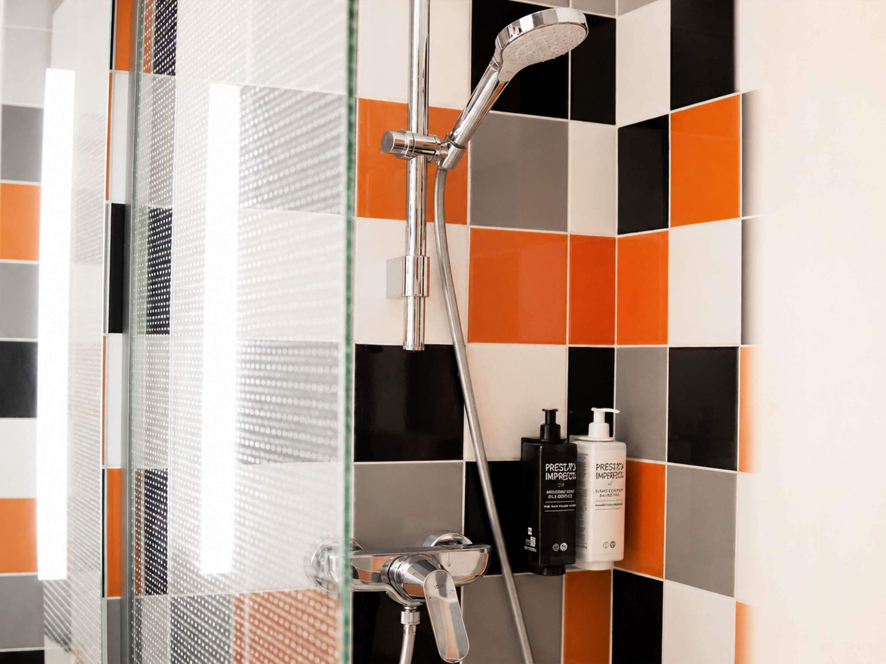 Ducha con cabezal de ducha manual, puerta de cristal y pared de azulejos naranja y negro.