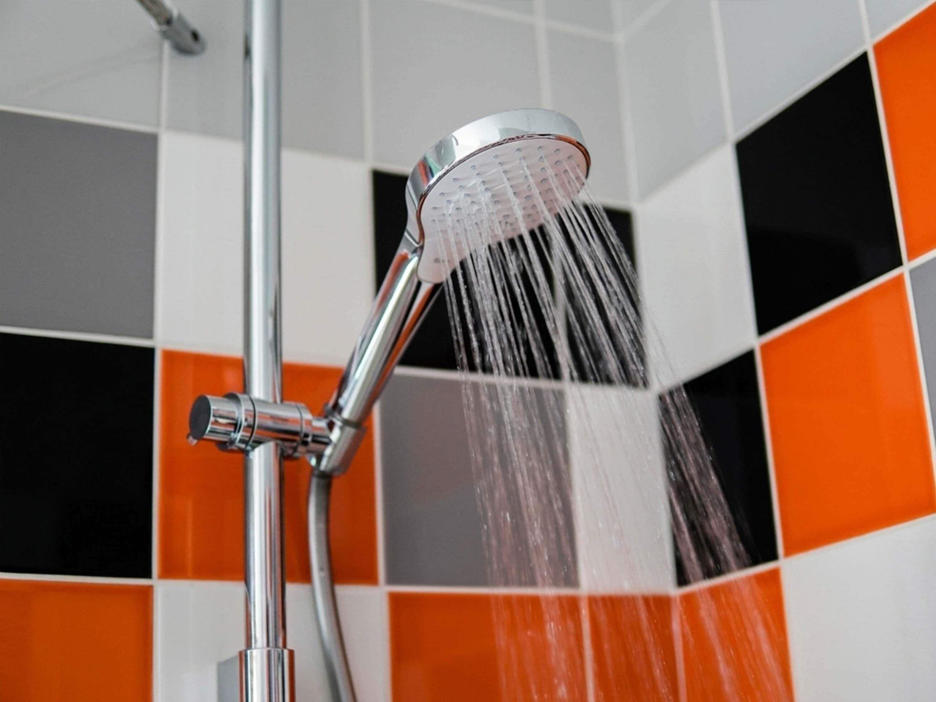 Una ducha con agua corriente, grifería cromada y pared de azulejos naranja y blanco.