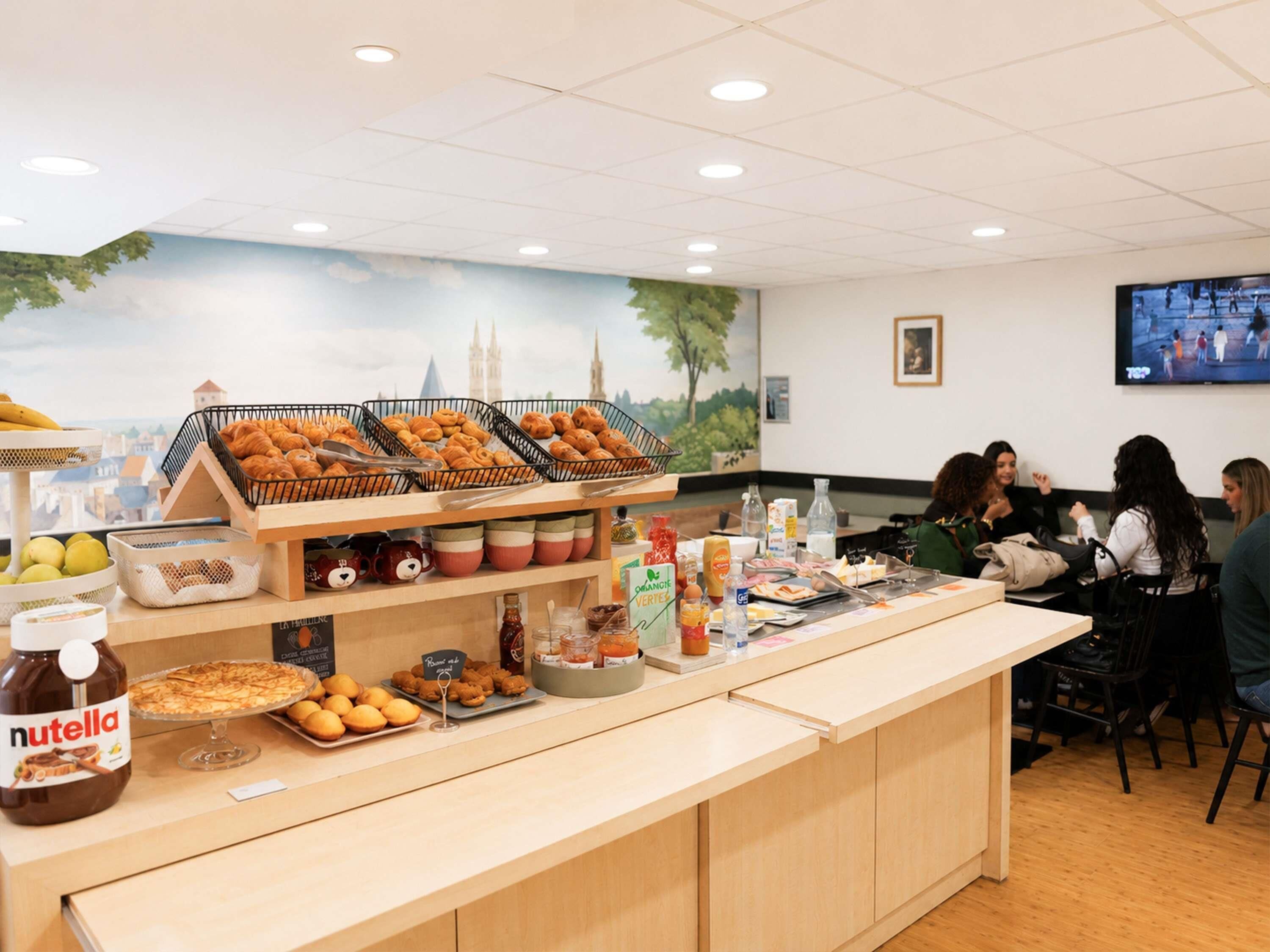 A buffet area with various food items, a Nutella jar, and a cityscape mural on the wall.