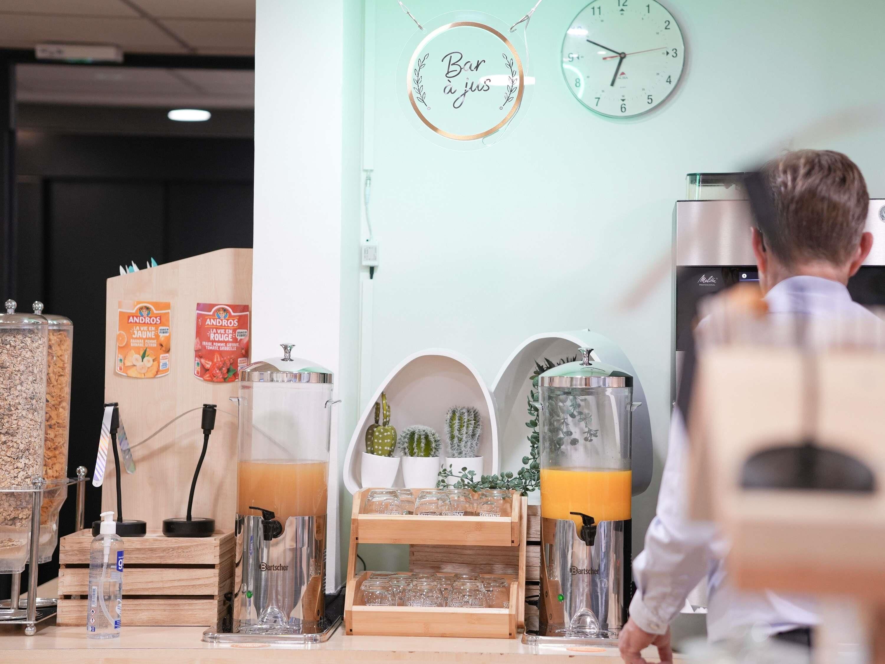 A café with a clock, a juice dispenser, and a coffee machine.