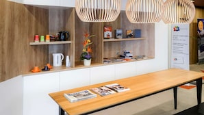 A reception area with a wooden reception desk, a coffee machine, and a shelf with magazines and a plant. - ibis Styles Caen Centre Historique (Caen)