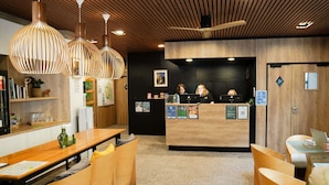 A reception area with wooden furniture, pendant lighting, and a counter with staff. - ibis Styles Caen Centre Historique (Caen)