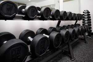 A rack of dumbbells with weight markings, arranged on a shelf in a gym setting.