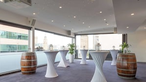 Une salle de conférence moderne, dotée de tables blanches, de barils en bois et de plantes en pot.