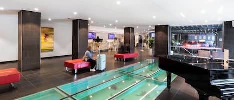 A lobby with a glass pool, a grand piano, and seating areas.