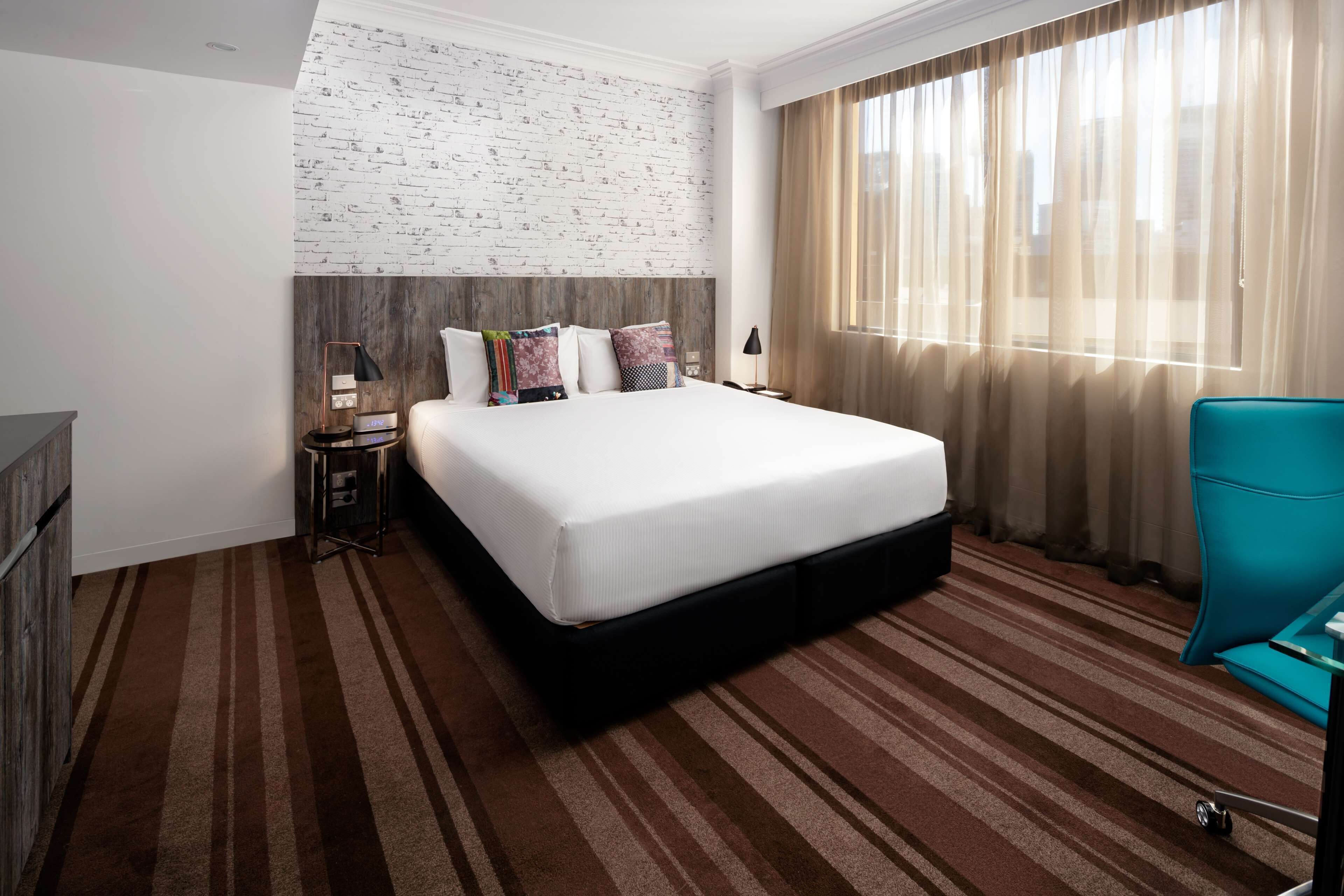 A hotel room with a large bed, a nightstand, a lamp, a chair, and a window with curtains.